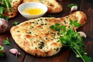 Indian naan bread with garlic butter on wooden table.